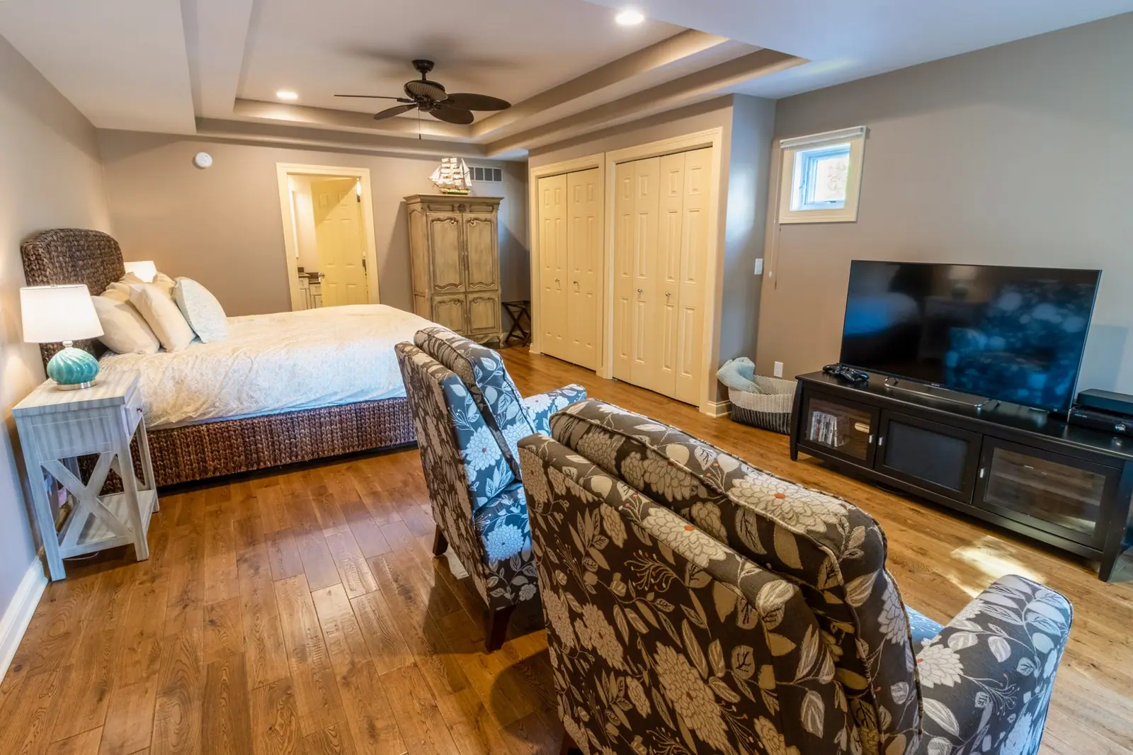 First-floor master bedroom with a king bed, two armchairs, a TV and an armoire under a tray ceiling