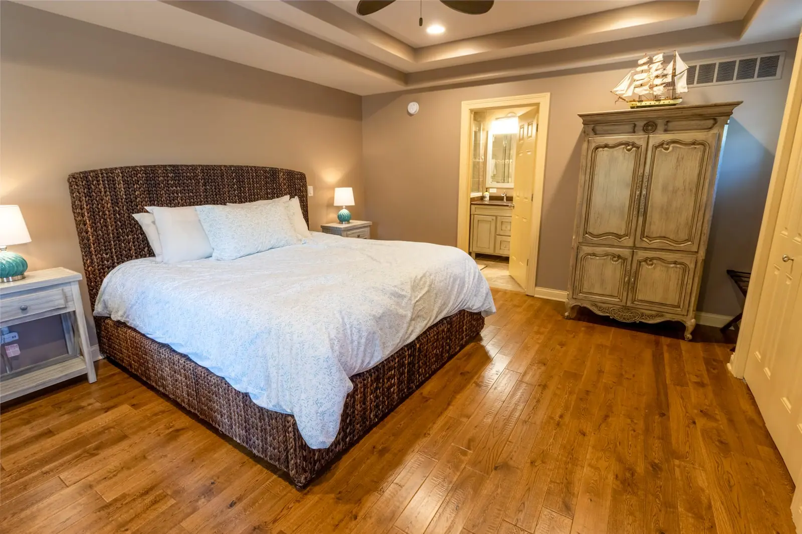 King bed with a woven headboard and a carved armoire in the first-floor master