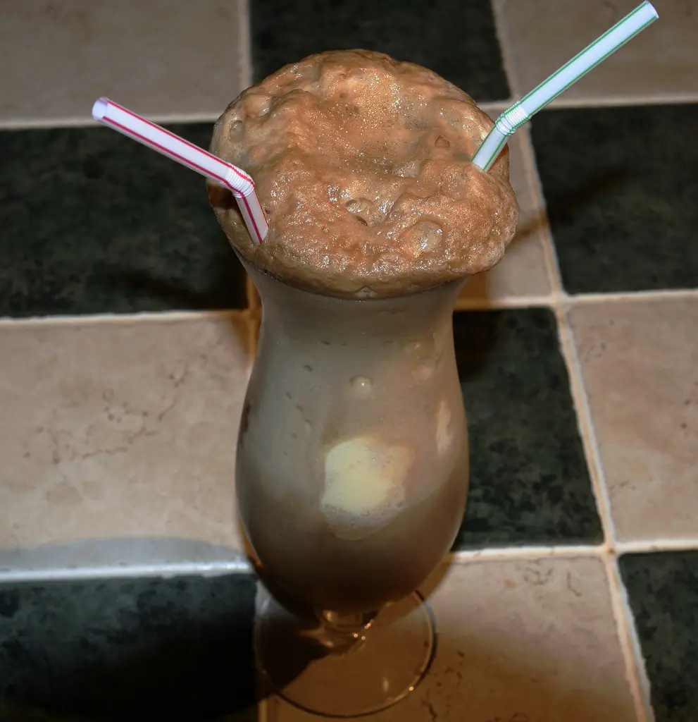 A root beer float with two straws in a tall glass