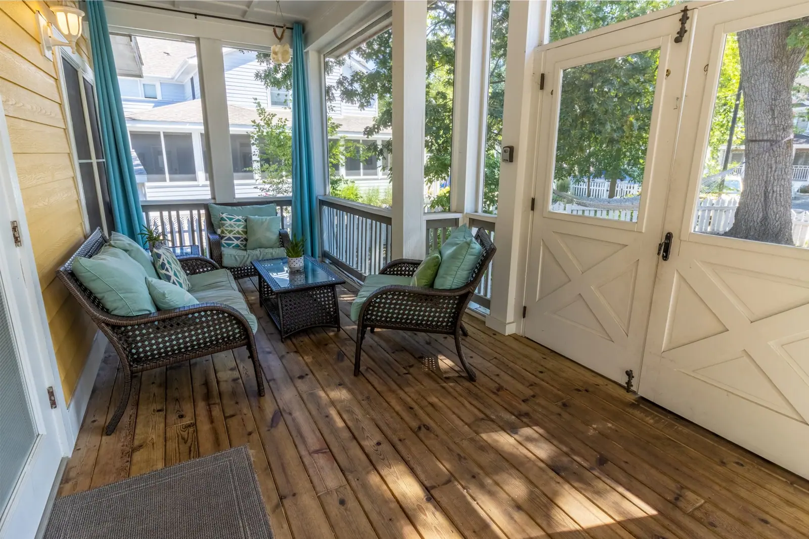 Front screened porch with wicker lounge chairs and a coffee table beside the white entry doors