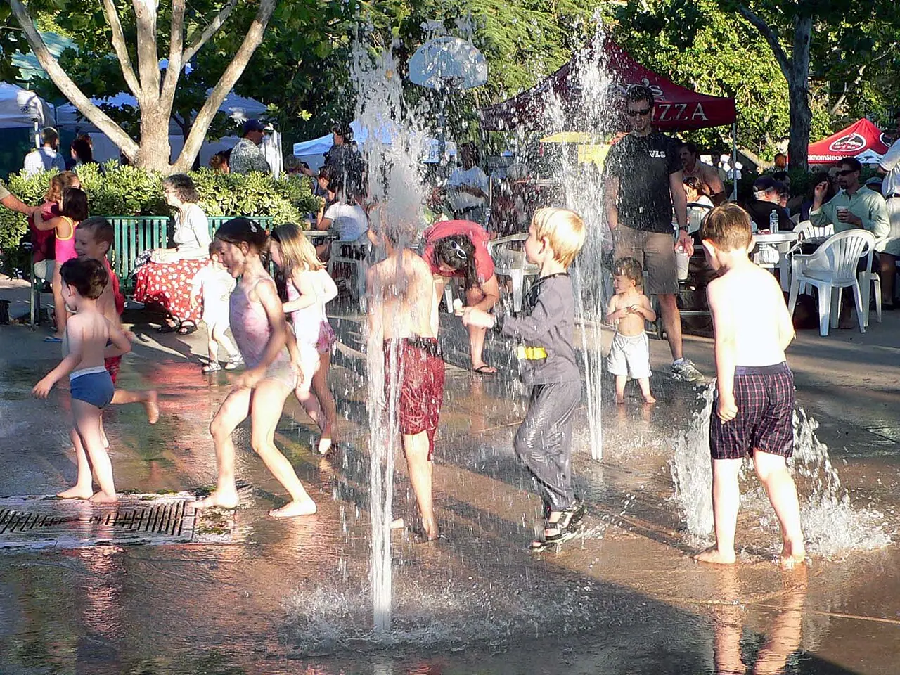 Children running through the jets of a splash-pad fountain on a summer evening