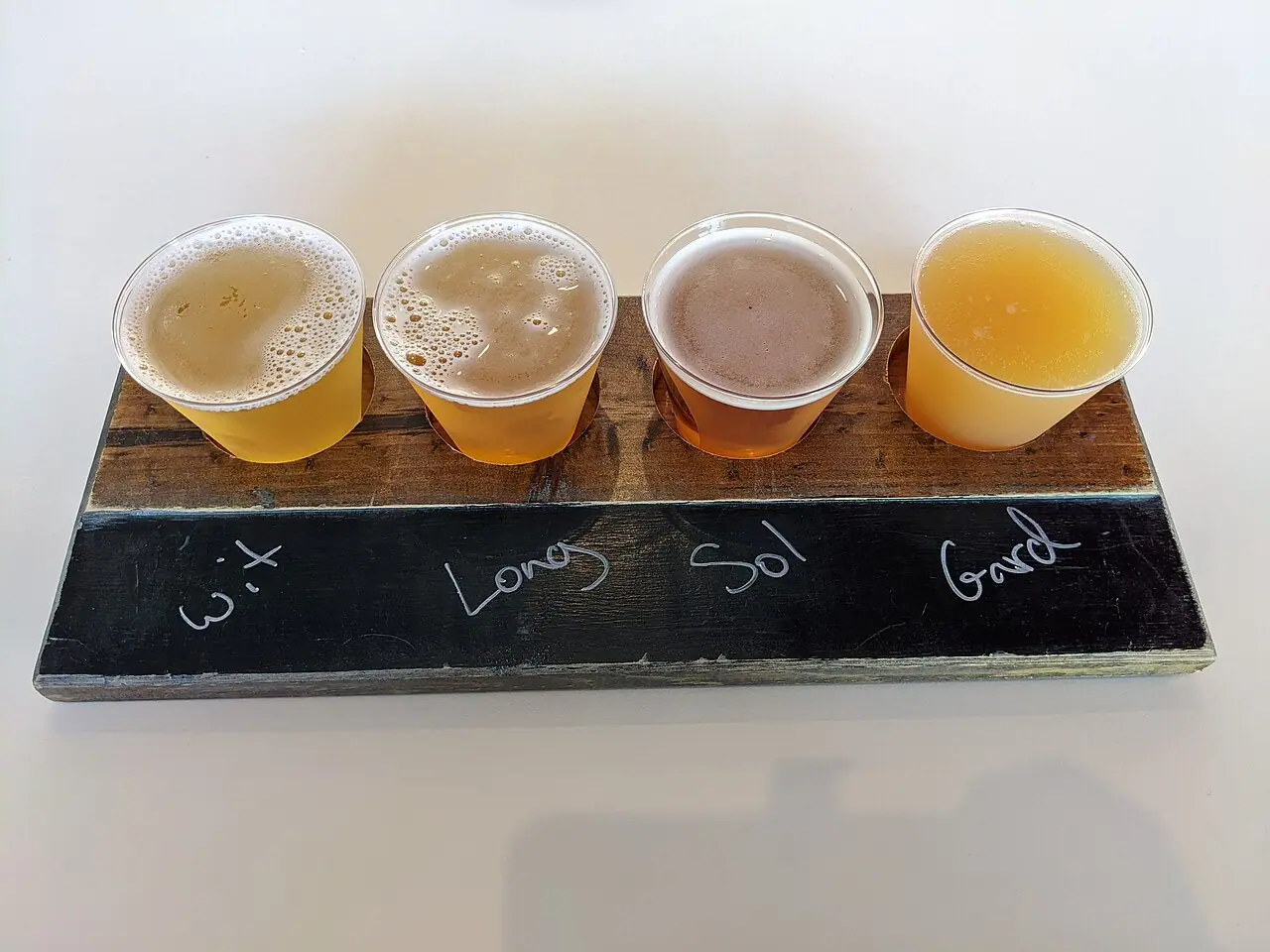 A flight of four craft beers on a wooden paddle