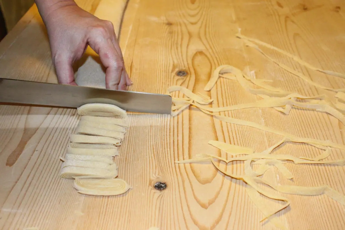 Fresh egg pasta being cut by hand on a wooden board