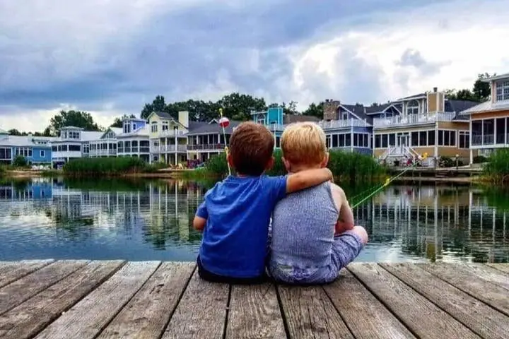 Two kids sitting together on a dock looking across Lake Kai to the cottages
