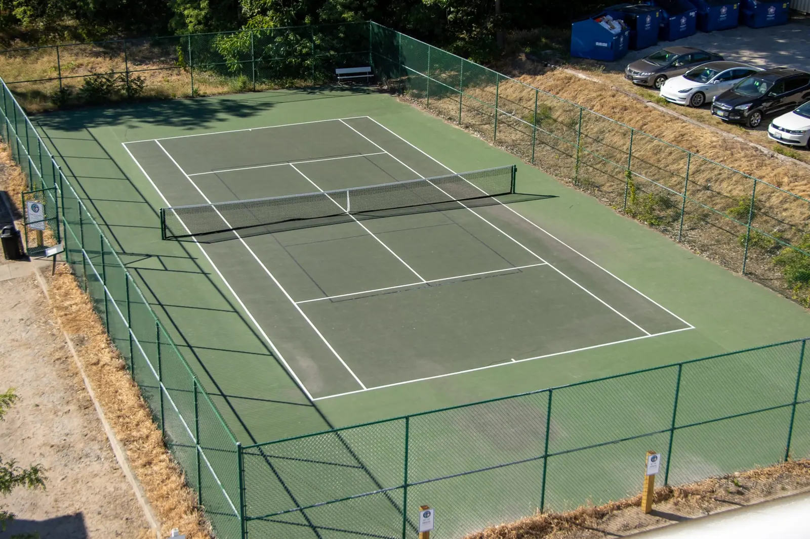 Fenced green tennis court among the trees