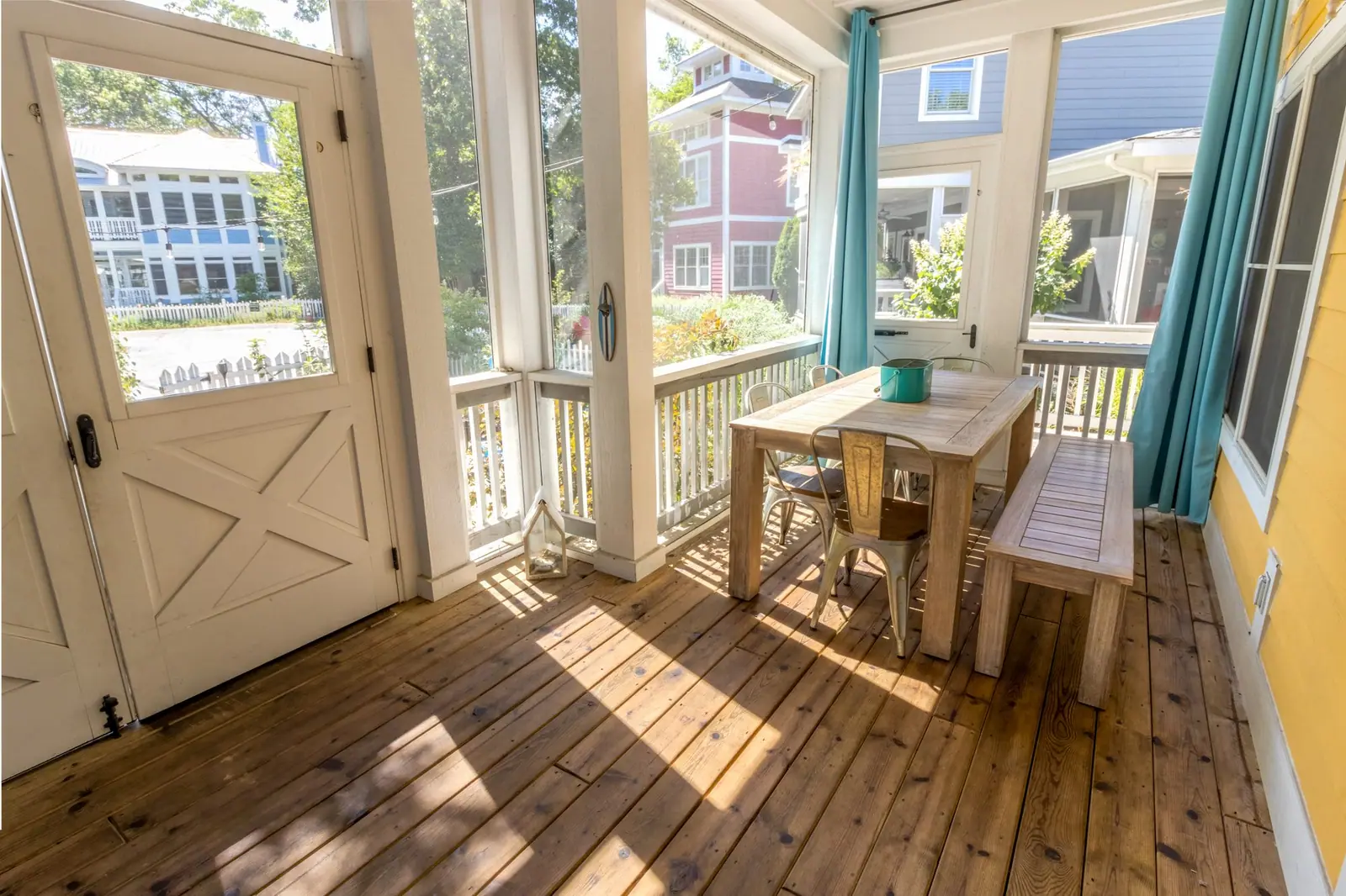 Sunlit screened porch with a farmhouse table, metal chairs and a wood bench